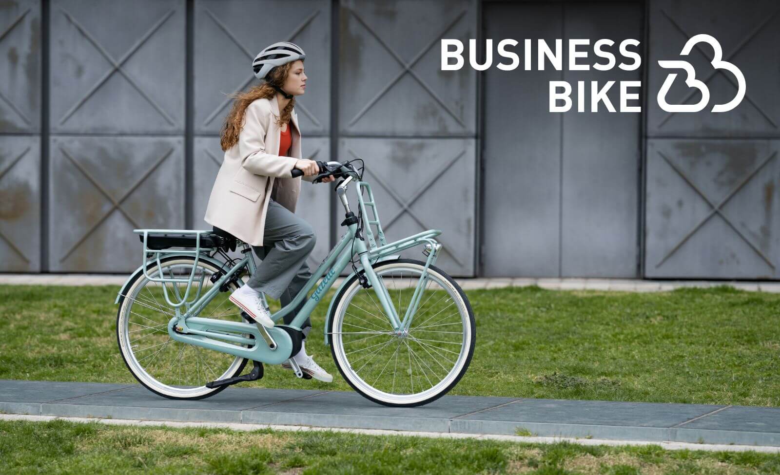 Frau auf einem grünen E-Bike von Gazelle fährt im Freien, trägt Helm und Business-Kleidung, Markenlogo "Business Bike" sichtbar.