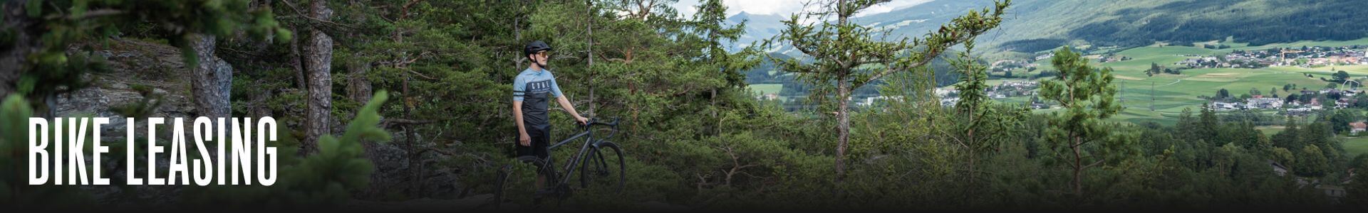Person mit Fahrrad im Wald, schaut auf hügelige Landschaft. Text: "Bike Leasing". Ideal für Natur- und Radsportbegeisterte.