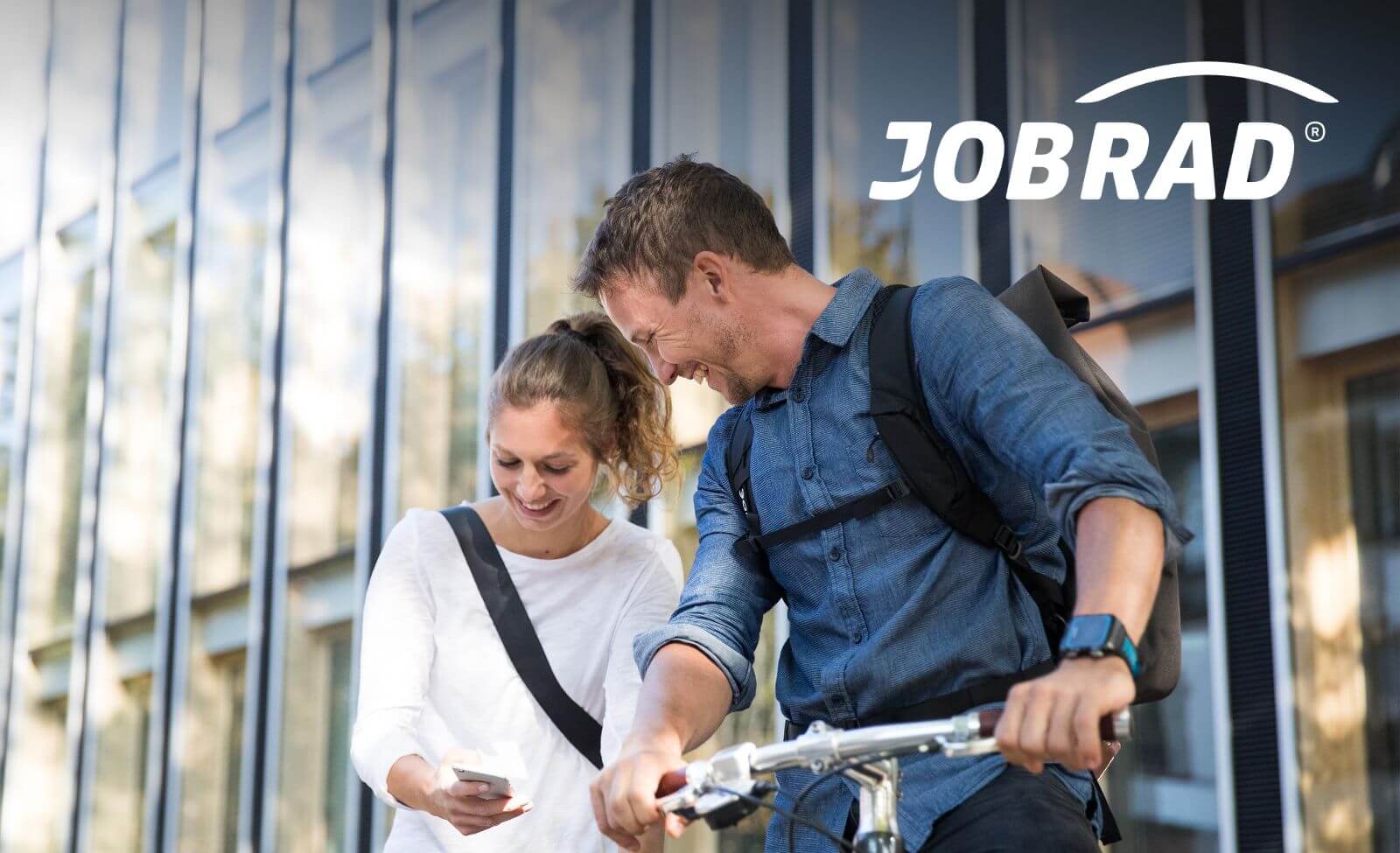 Zwei Personen stehen vor einem Bürogebäude, ein Mann hält ein Fahrrad. JobRad-Logo darüber.